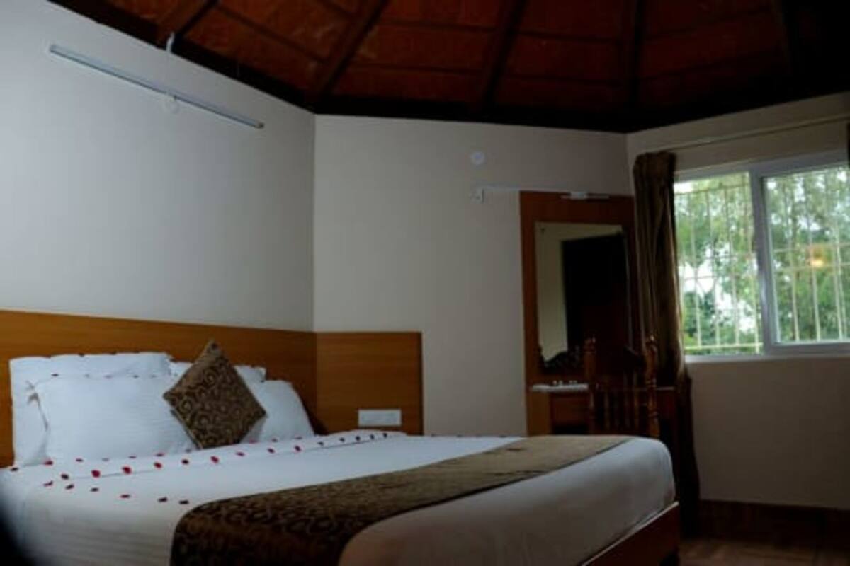 A hotel room with a bed, a wooden headboard, a window with curtains, and a ceiling fan.