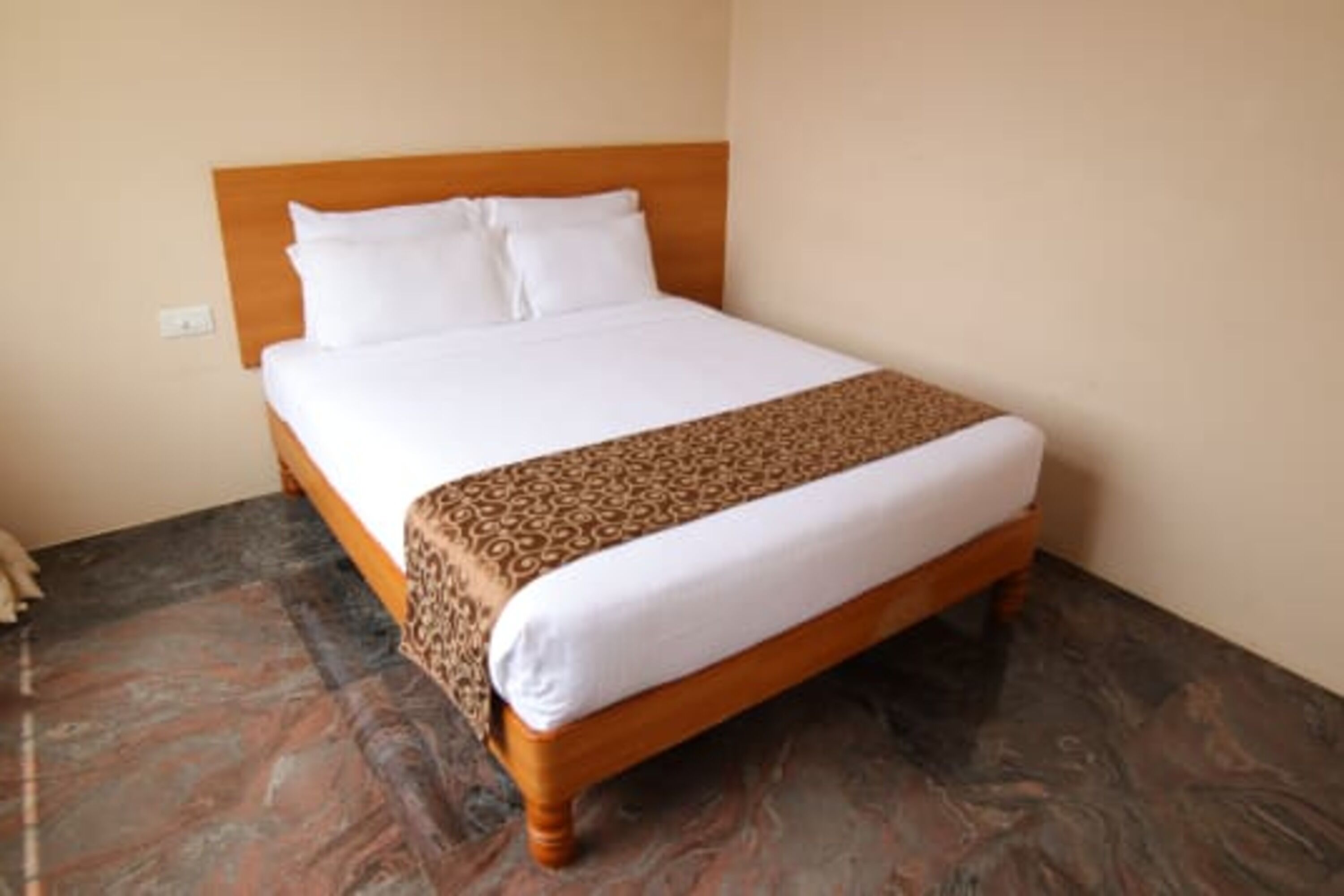A neatly made bed with a wooden headboard, a patterned bedspread, and a marble floor.