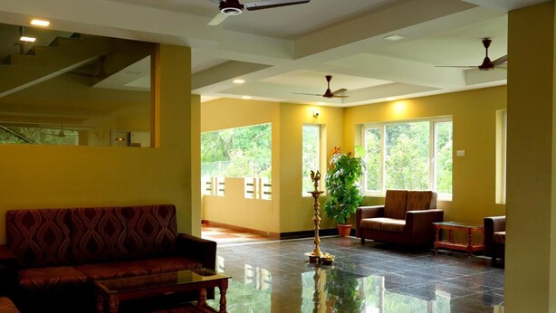 A spacious living area with a reflective floor, a sofa, a chair, and a potted plant. - Ack Palacce Inn (Yercaud)