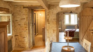 A rustic room with exposed stone walls, a wooden table with a metal lamp, and a window with a view. - Dreamy Retreat in Loubejac (Loubejac)