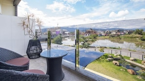 A balcony with wicker furniture, a glass table, and a view of a lake and buildings in the distance. - WMS Villa (Sanxing)