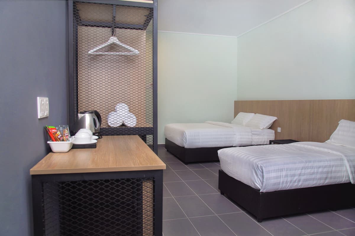 Habitación de hotel con dos camas, una mesa de madera, un hervidor y un perchero.