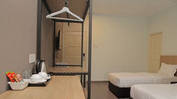 A hotel room with a wooden table, two beds, a hanging clothes rack, and a small kitchenette area.