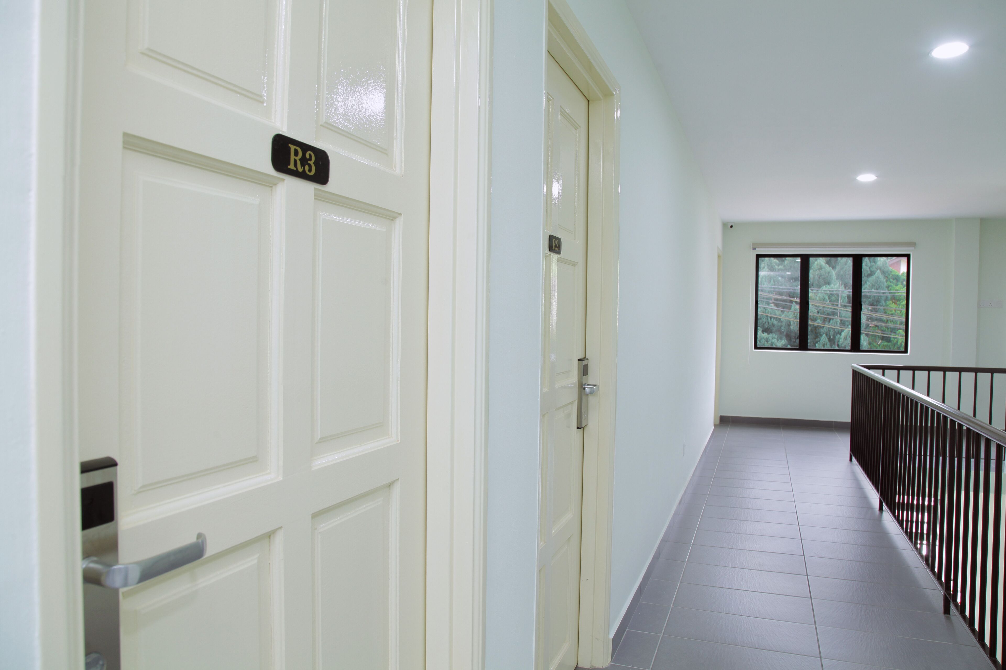 A corridor with white doors, a metal handrail, and a window with a view of trees.