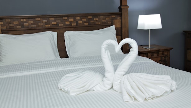 Ein ordentlich bezogenes Bett mit weißen Kissen und einer Herz-Form-Handtuchanordnung.