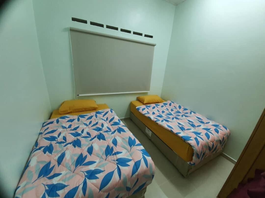 A room with two single beds, each with a patterned bedspread and a yellow pillow. There is a window with a white blind covering the upper part of the window.