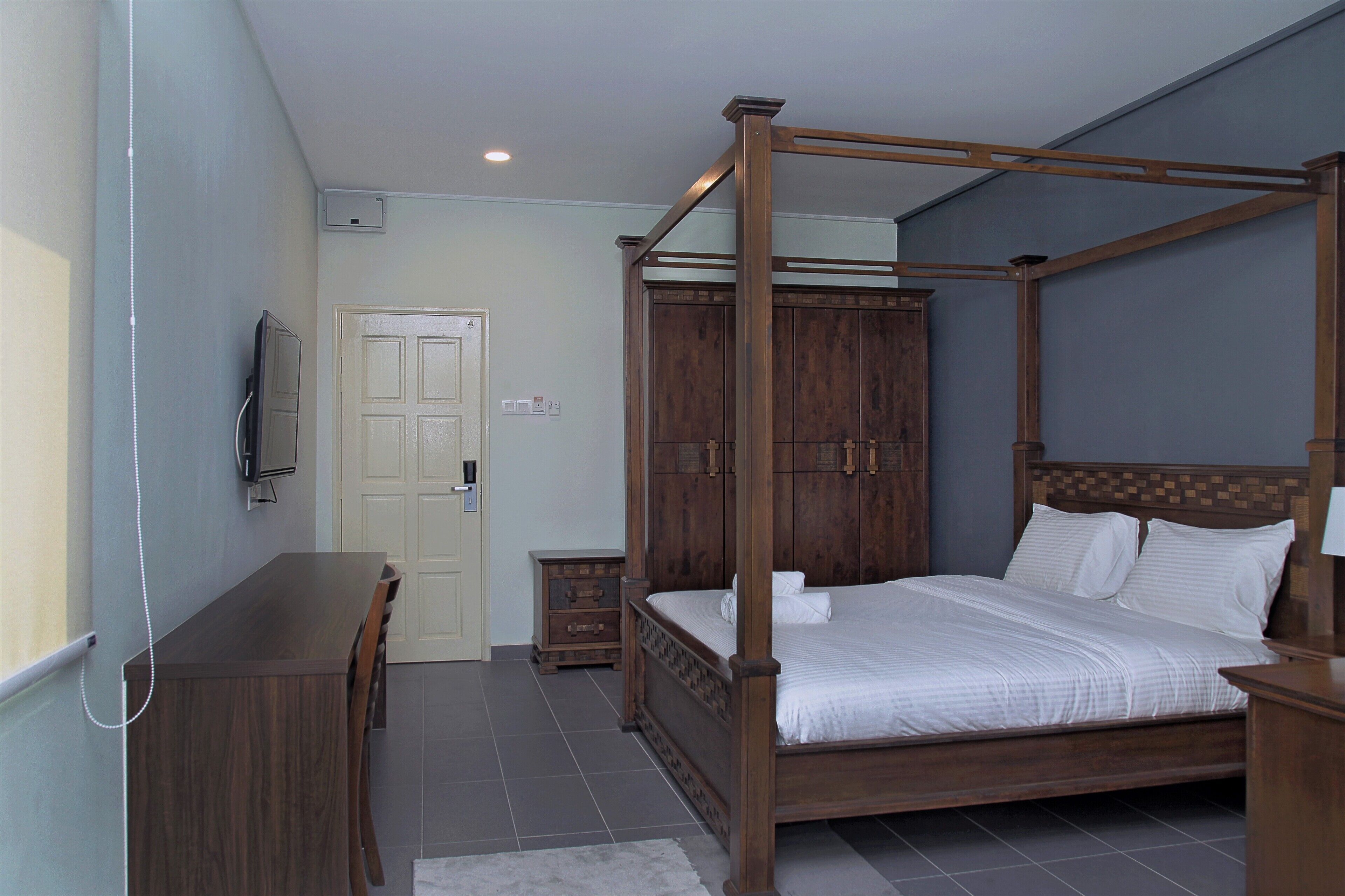 A four-poster bed with a wooden headboard, a bedside table, a small wooden nightstand, and a television mounted on the wall.