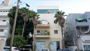 Un edificio de varios pisos con balcones, coches aparcados y palmeras.