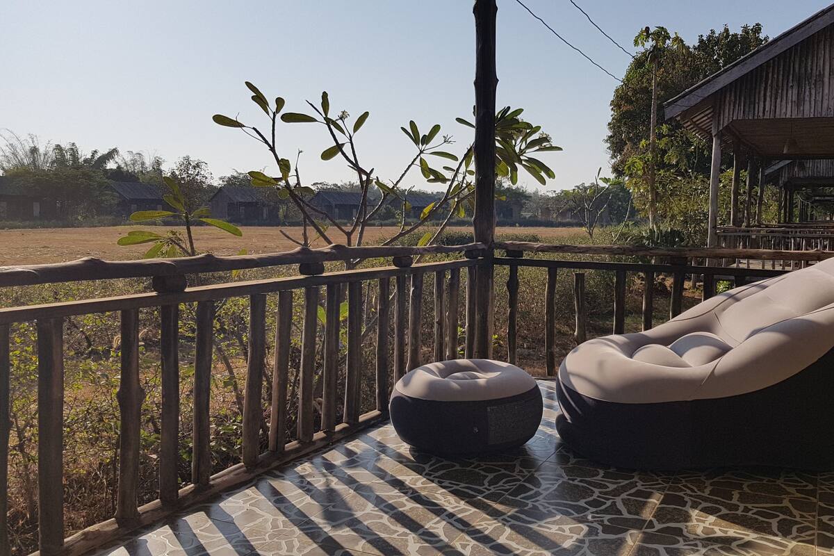 Una terraza de madera con zona de estar acolchada, suelo de baldosas y vistas a un paisaje rural.