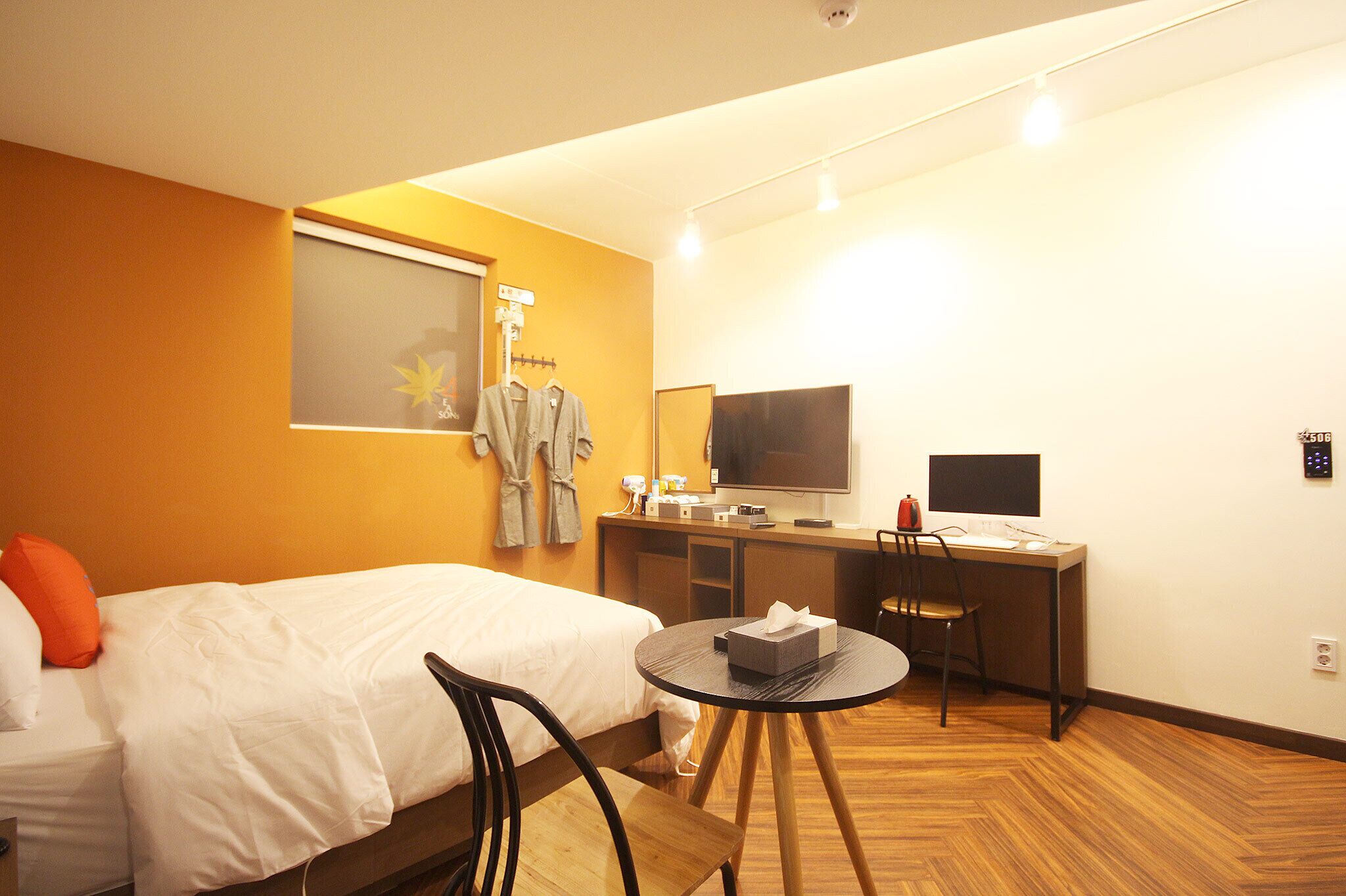 A hotel room with a bed, a desk, a chair, a television, and a small table with a tissue box.