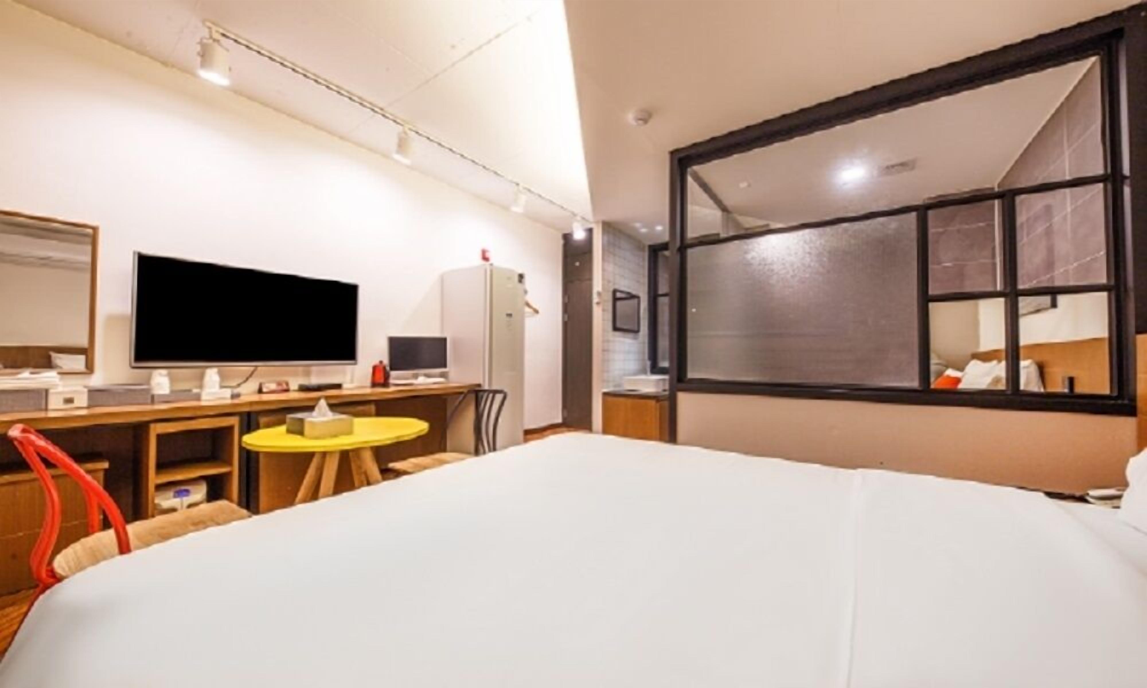 A hotel room with a bed, a desk with a computer, a small table, and a large window.