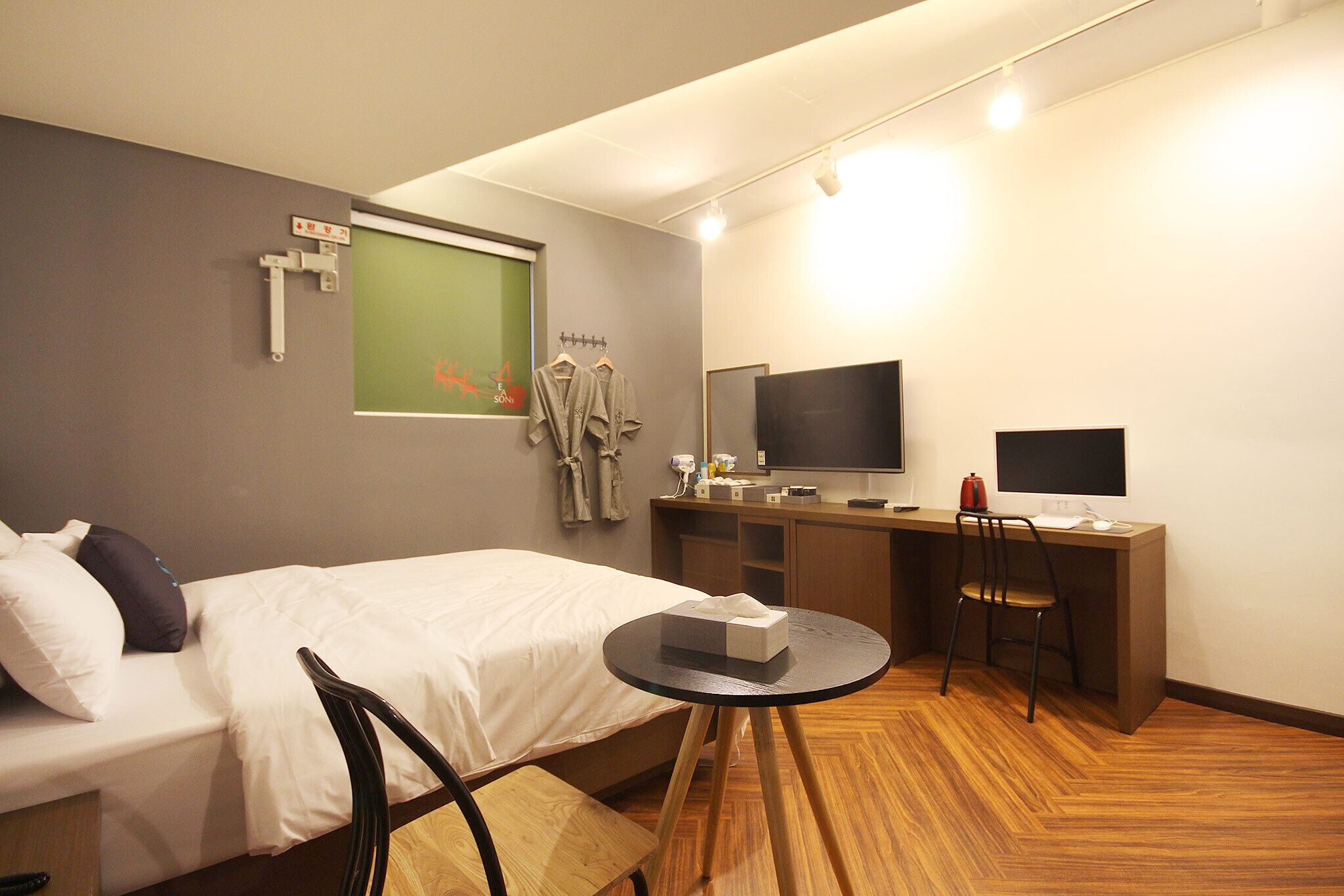 Une chambre d’hôtel avec un lit, un bureau équipé d’un ordinateur, une télévision et une petite table sur laquelle se trouve une boîte de mouchoirs.