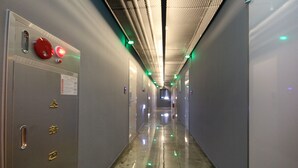 Un pasillo largo y estrecho con piso brillante, puertas a la izquierda y luces verdes en el techo.