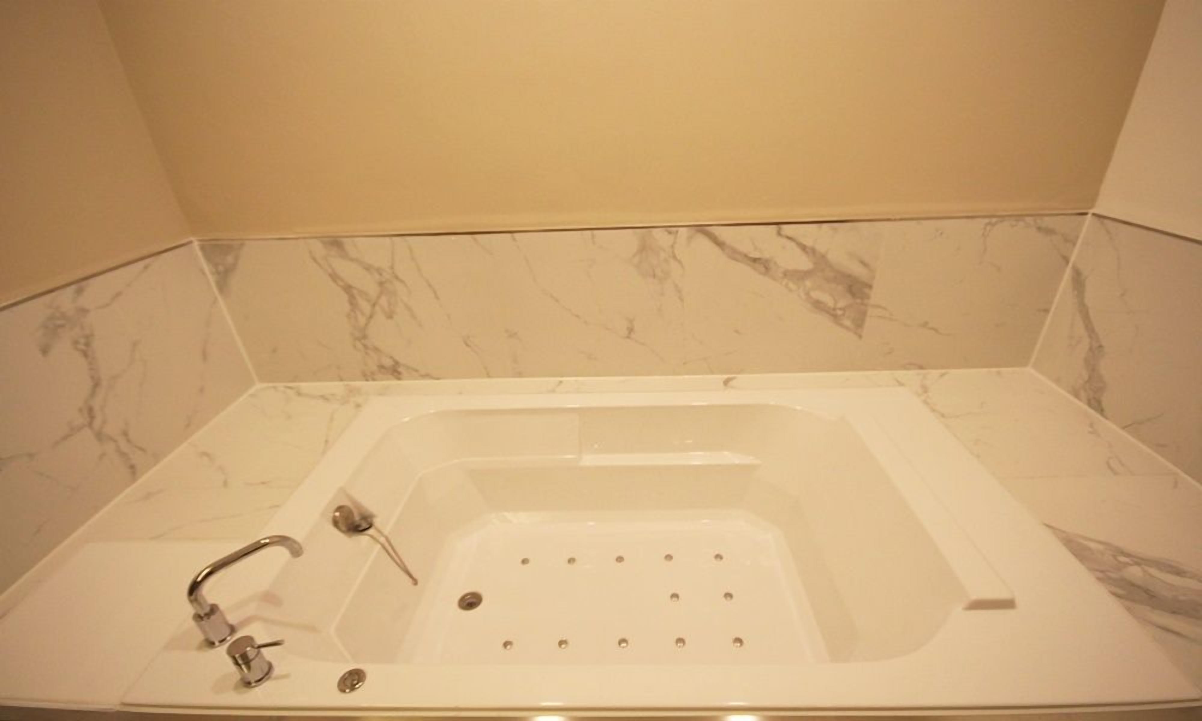 Un baño con una bañera independiente, un cabezal de ducha y un revestimiento de mármol.