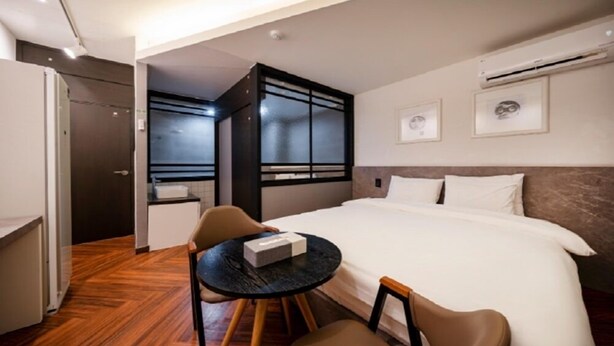 Una habitación de hotel con una cama, una pequeña mesa con sillas, un escritorio y una ventana.