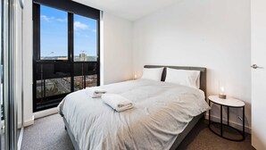 Moderni hotellihuone, jossa on suuri sänky, pieni yöpöytä ja suuri ikkuna, josta avautuu näkymä kaupunkiin.