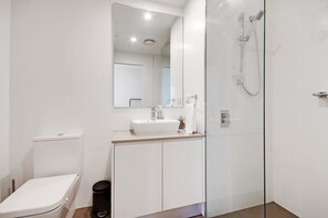 A modern bathroom with a toilet, sink, and glass-enclosed shower. - Swainson at Vue (Adelaide)