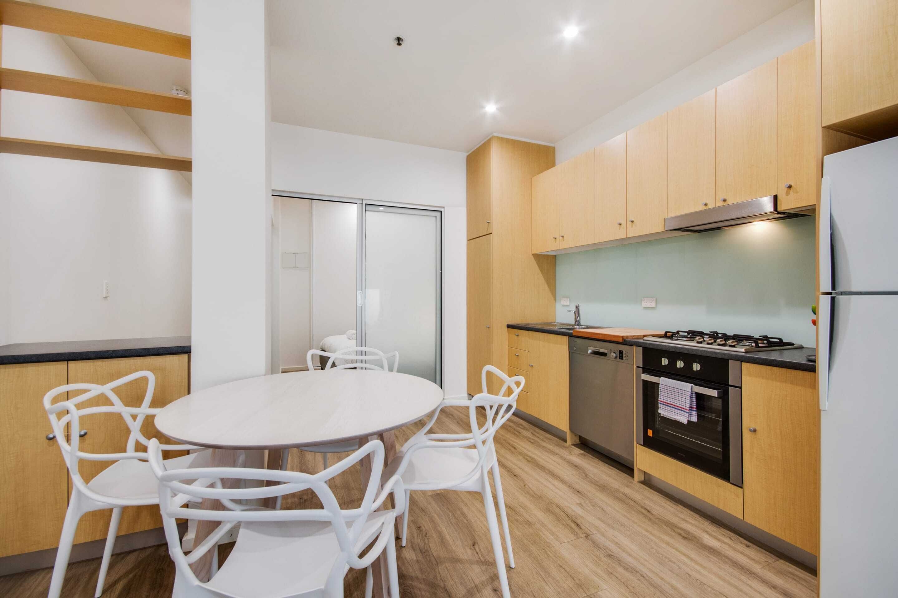Una cocina moderna con armarios de madera, estufa a gas y refrigerador. Hay una mesa de comedor con sillas blancas.