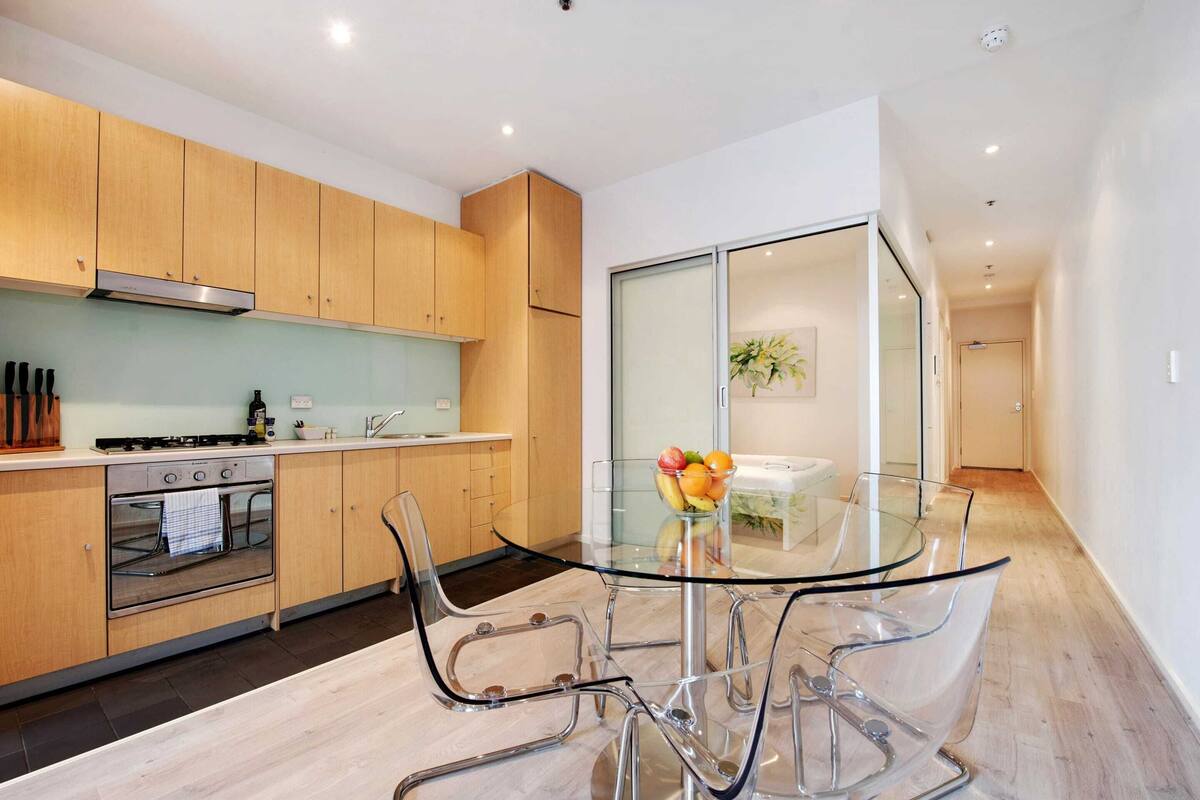 A modern kitchen with wooden cabinets, a glass-top dining table, and clear chairs.