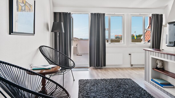 Ein modernes Wohnzimmer mit einem großen Fenster, einem schwarzen Sessel, einem Holztisch und einem Bücherregal.