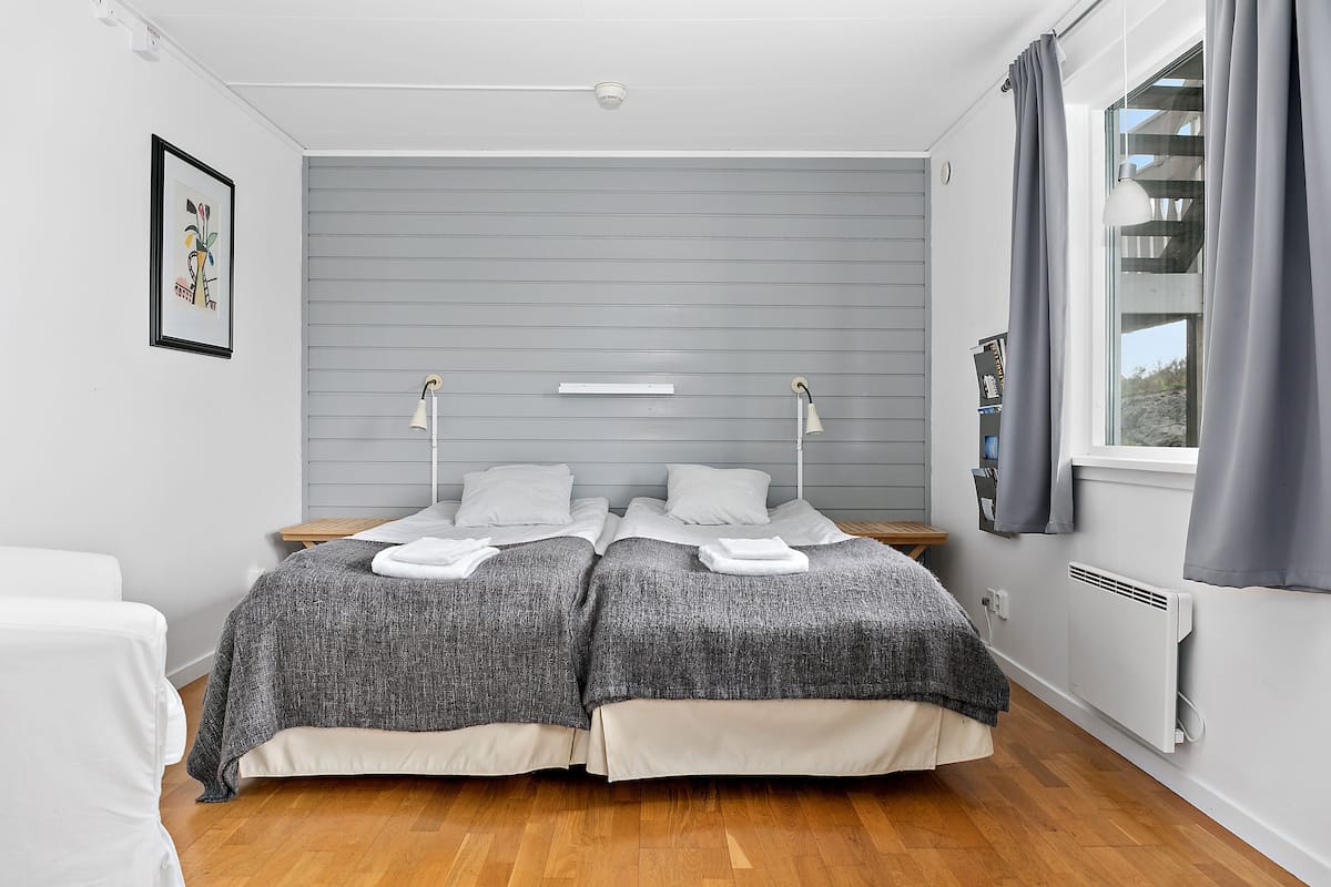 Une chambre avec deux lits, une fenêtre avec des rideaux, un radiateur et un tableau au mur.