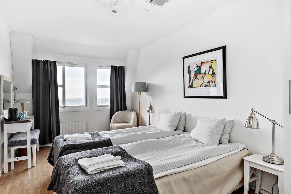 Une chambre d’hôtel avec deux lits, un bureau, une chaise, une lampe et un tableau au mur.
