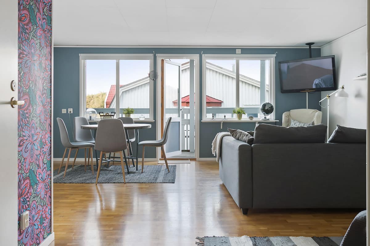 Un salon avec un canapé gris, une table à manger avec des chaises et un téléviseur fixé au mur.