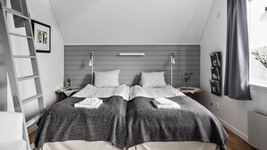 Ein Schlafzimmer mit zwei Betten, einer Leiter, einem Nachttisch mit einem Buch und einem Fenster mit Vorhängen.