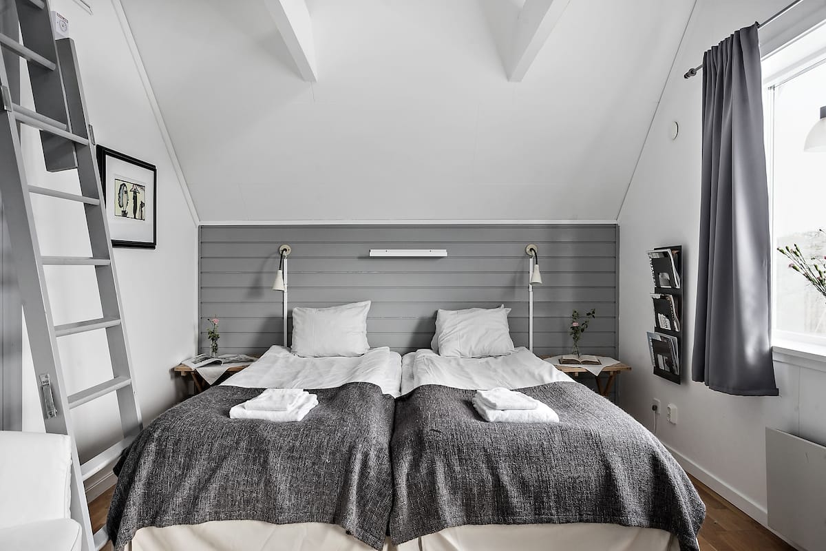 Une chambre avec deux lits, une échelle, une table de chevet avec un livre et une fenêtre avec des rideaux.
