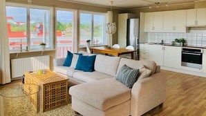 Ein modernes Wohnzimmer mit Sofa, Esstisch und Küchenbereich mit weißen Schränken und einem Edelstahl-Kühlschrank.