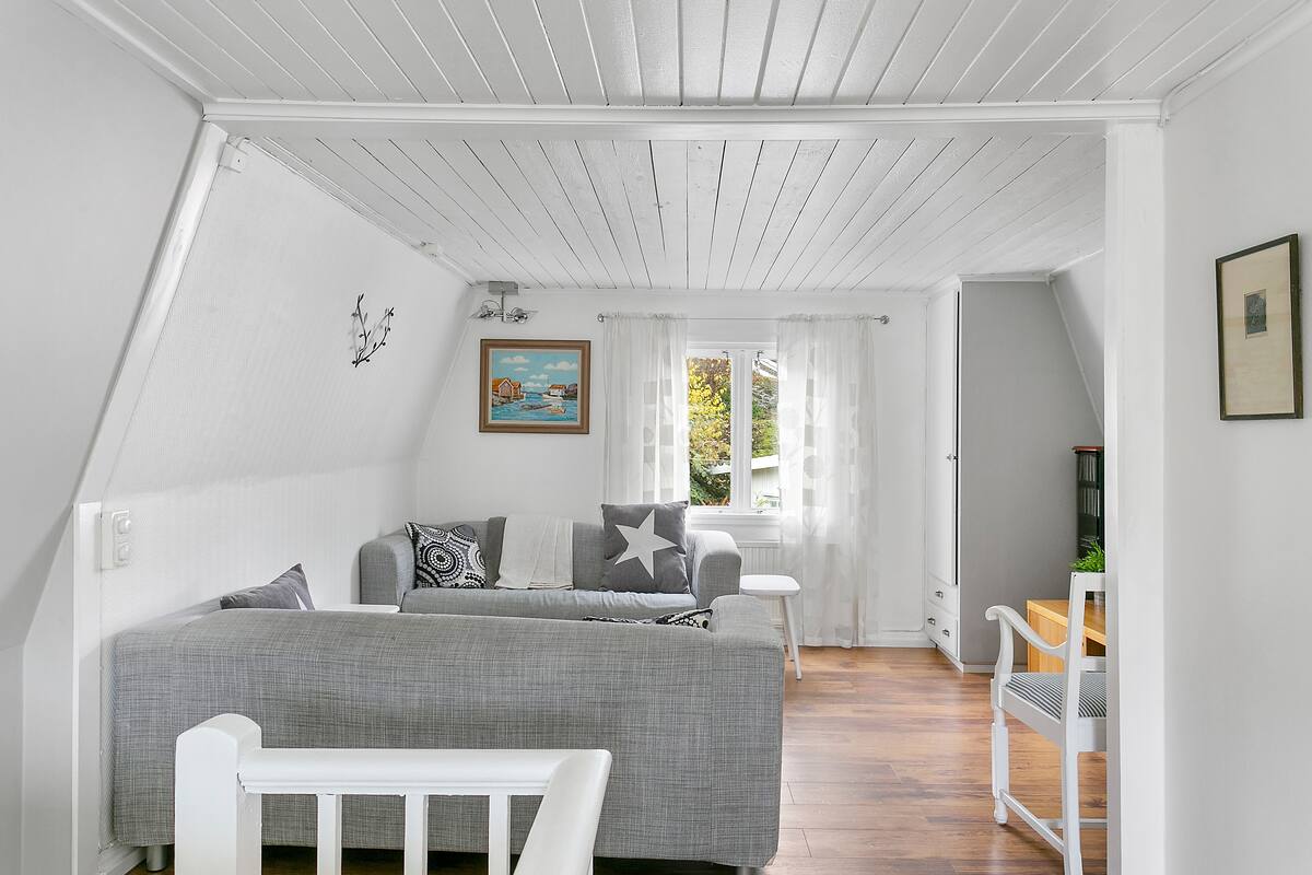 Une pièce avec un lit en mezzanine, une petite table et une chaise. Il y a une fenêtre avec des rideaux et un tableau au mur.