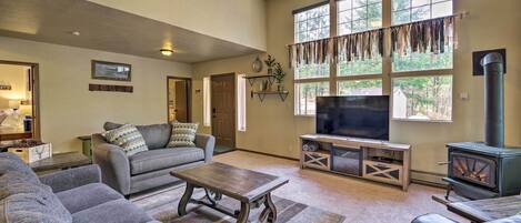A spacious living room with a fireplace, large windows, and a ceiling fan.