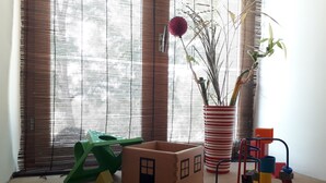 Una mesa de madera con una casita de juguete, un florero y una planta en una maceta a rayas.