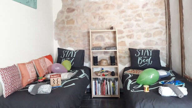 Una sala de estar acogedora con una pared de piedra, dos sofás con cojines estampados, una estantería y un techo de madera.