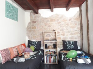 Uma sala de estar acolhedora com uma parede de pedra, dois sofás com almofadas estampadas, uma estante de livros e teto de madeira.