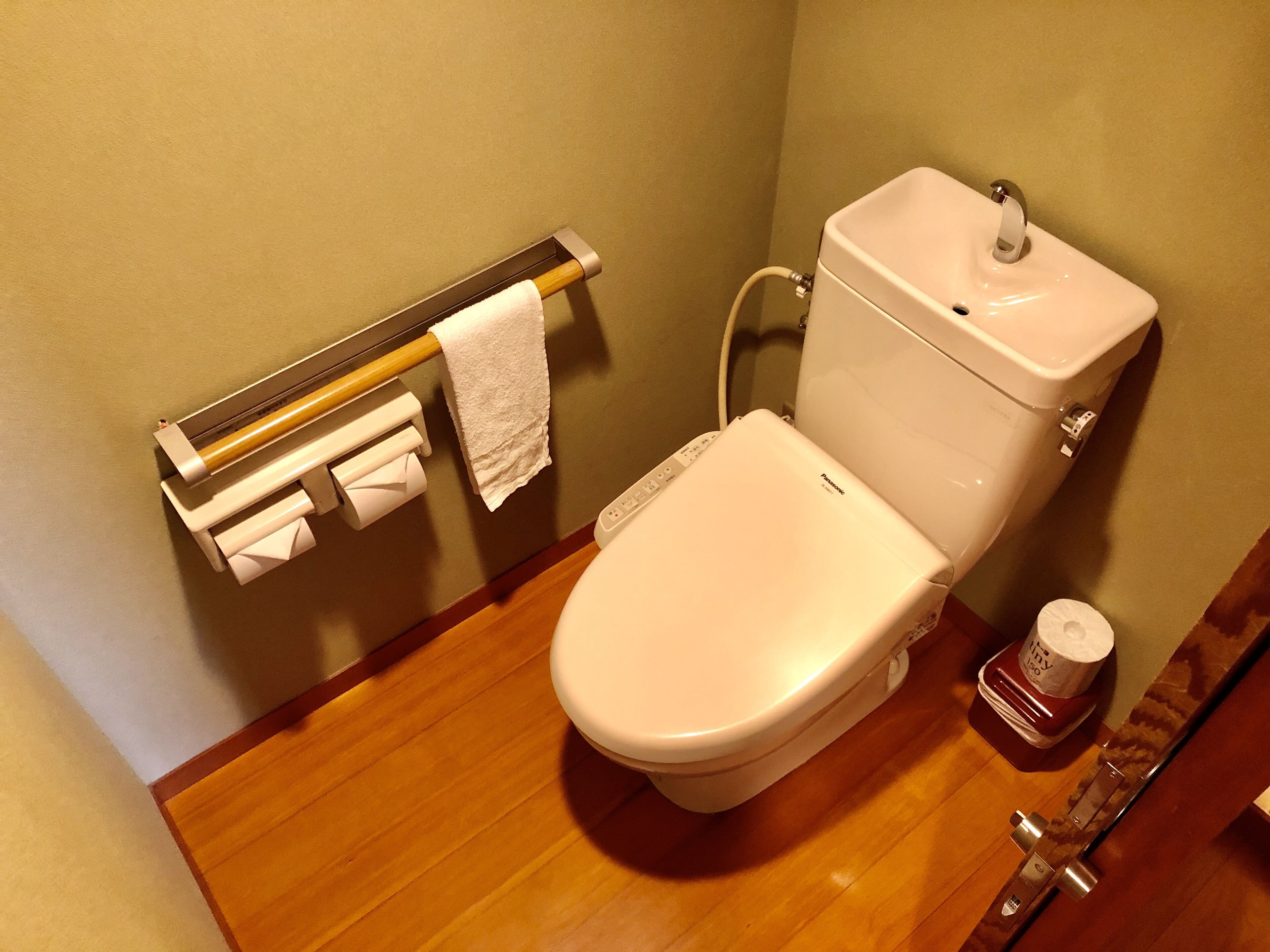 A bathroom with a toilet, a paper towel dispenser, and a toilet paper roll.