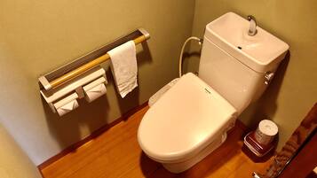 A bathroom with a toilet, a paper towel dispenser, and a toilet paper roll.