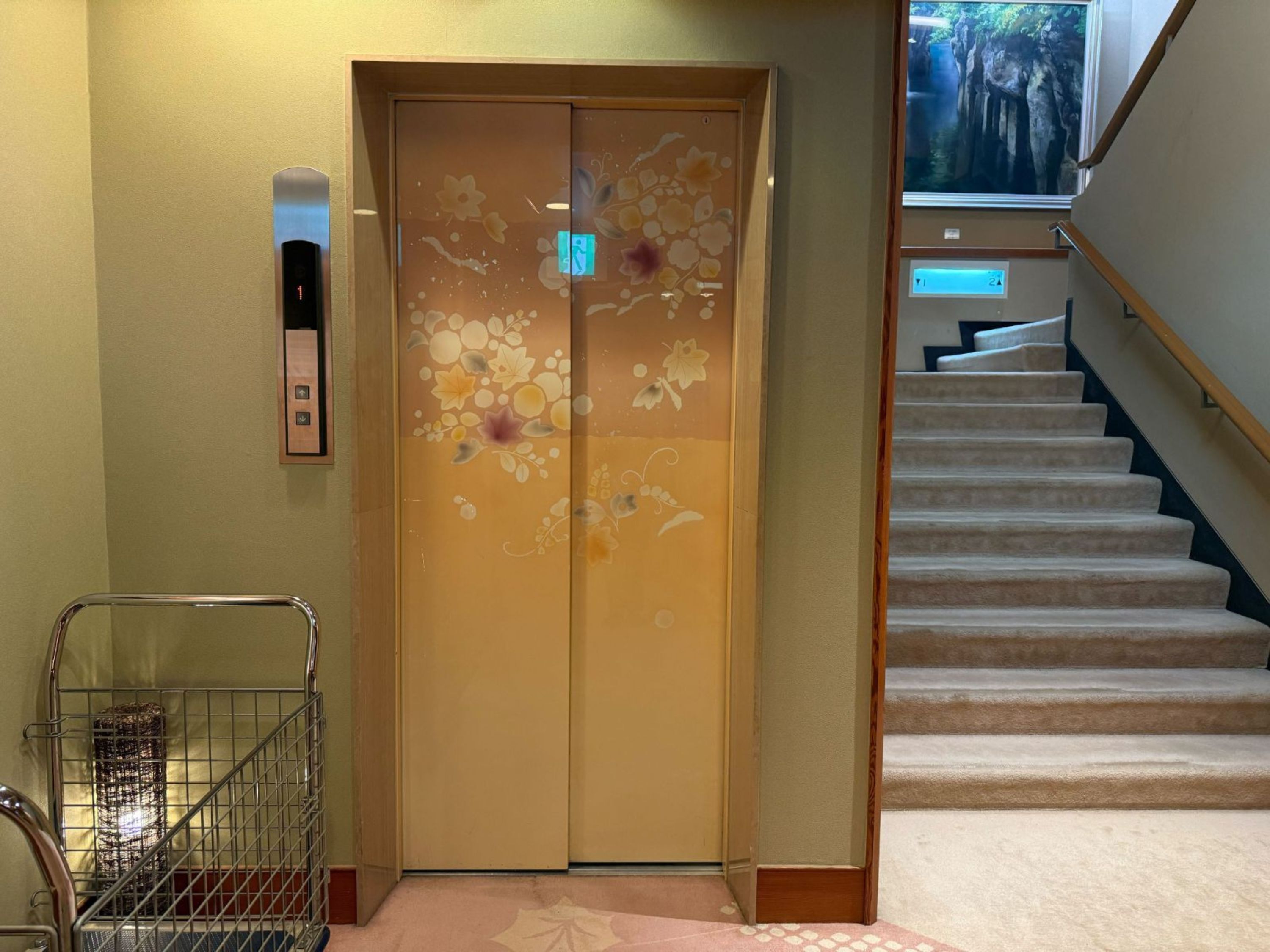 An elevator with floral designs, a digital display, and a staircase with carpeted steps.
