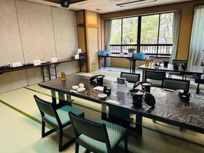 Un salón de conferencias con tatamis, mesas cubiertas con plástico negro y juegos de té japoneses tradicionales.