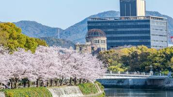 Vista del río con cerezos en flor, un puente y edificios modernos al fondo.