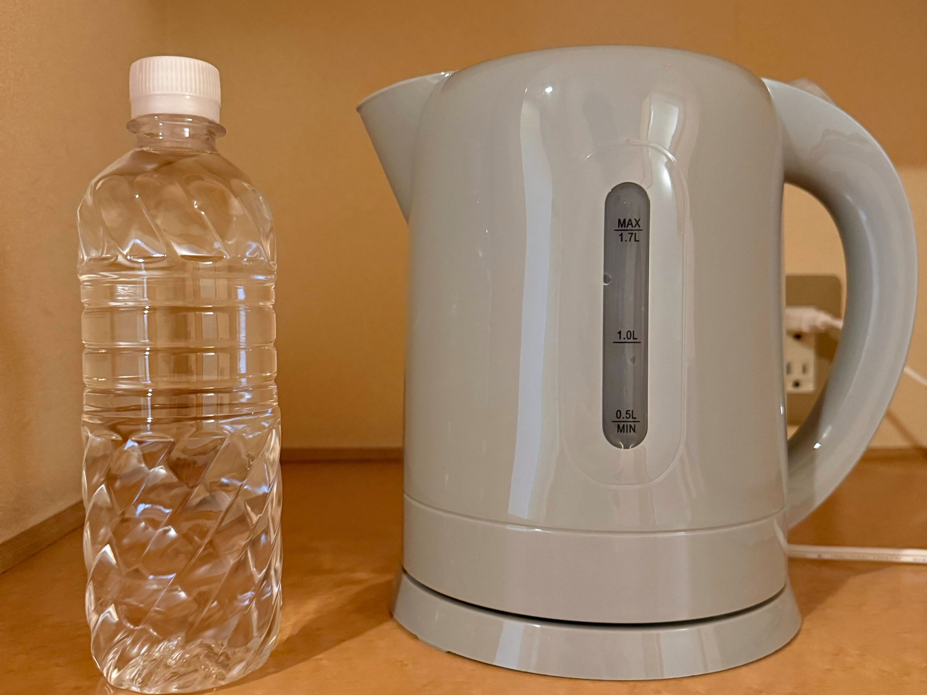 A clear plastic water bottle and a white electric kettle with measurement markings on a countertop.