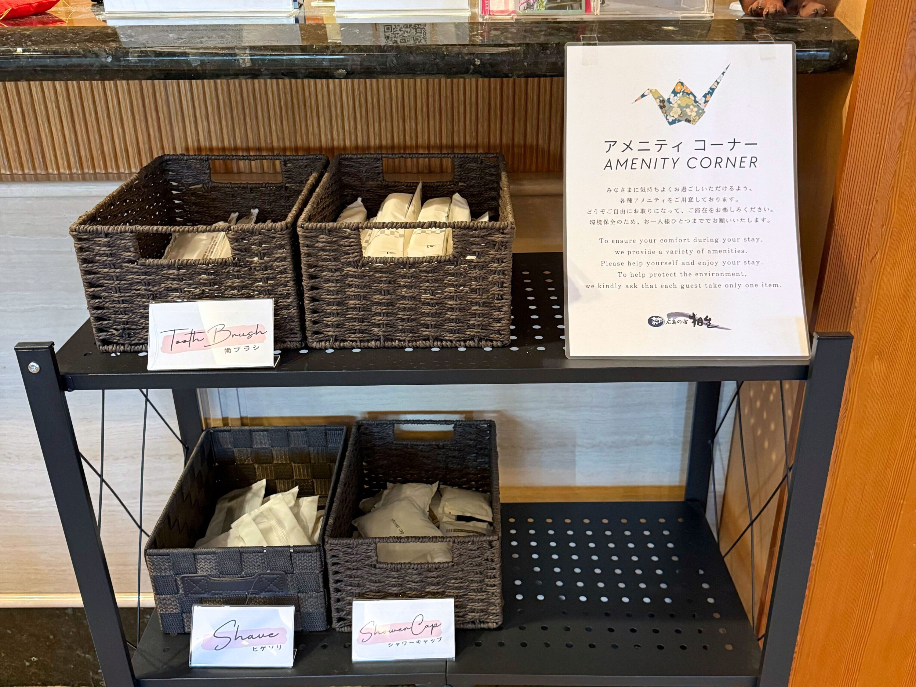 A hotel reception area with amenities labeled in both English and Japanese, including toothbrushes, a shower cap, and a sign promoting environmental protection.