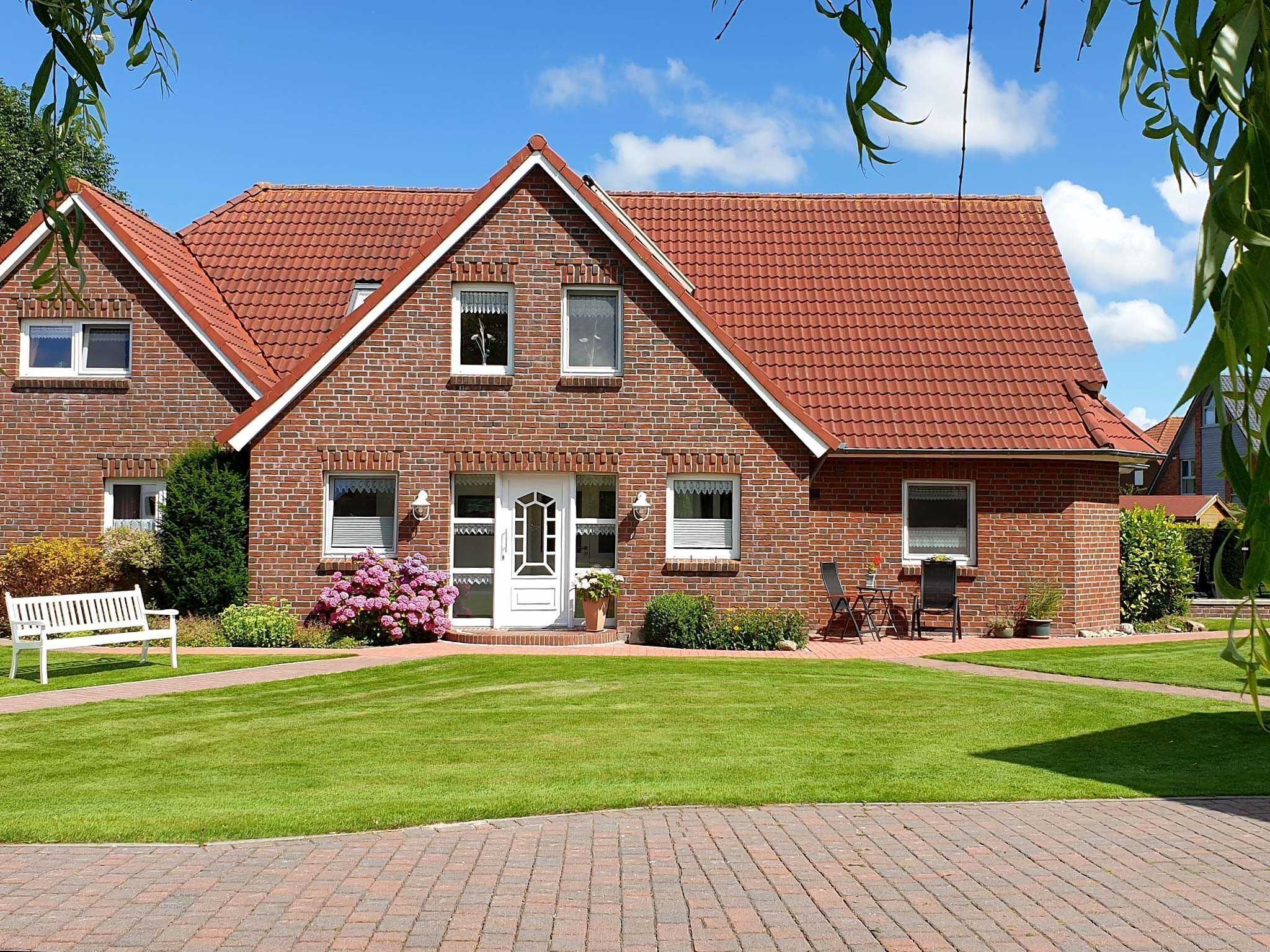 Een herenhuis met twee verdiepingen, met een rode pannendak, een voortuin en een verzorgd gazon.