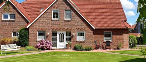A two-story brick house with a red-tiled roof, a front porch, and a well-maintained lawn.