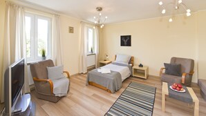 A modern hotel room with a bed, two armchairs, a TV, and a dining table with fruit. - Victus Apartamenty - Chopin 2 (Sopot)