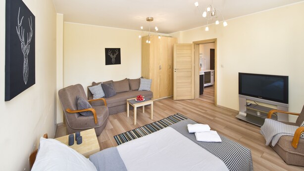 A modern living room with a sofa, armchairs, a coffee table, a TV, and a dining area. - Victus Apartamenty - Chopin 2 (Sopot)