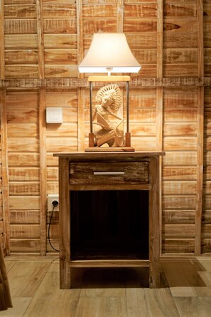 A rustic cabinet with a lamp and drawer, situated against a wooden wall.