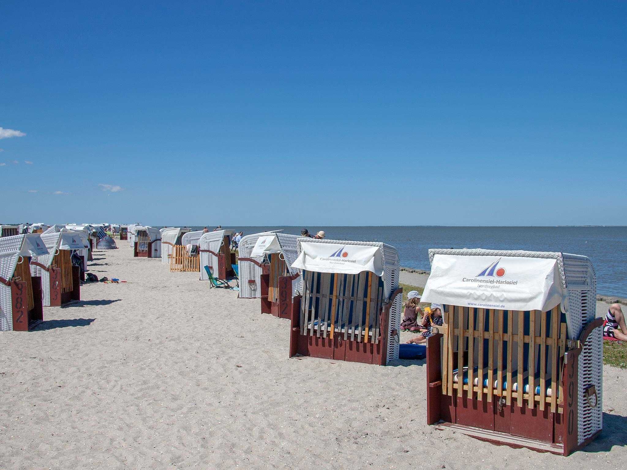 Strandhütten mit weißen Markisen und Holzwerteln, die an einem Sandstrand aufgereiht sind.