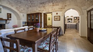 A dining area with a long wooden table, chairs with floral cushions, and a stone ceiling. - Charming Trulli with Pool for 8 people in Monopoli’s countryside (Monopoli)