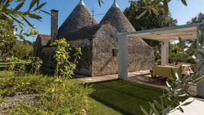 A stone building with conical roofs, a covered patio area, and a well-maintained garden. - Charming Trulli with Pool for 8 people in Monopoli’s countryside (Monopoli)
